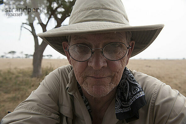 Nahaufnahme eines Mannes draußen im Queen-Elizabeth-Nationalpark  der einen Hut  ein Kopftuch und eine Brille trägt; Uganda