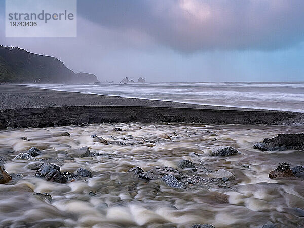 Küstenlinie des Strandes Motukiekie bei Sonnenuntergang  mit dramatischen Gewitterwolken und silhouettierten Felsformationen in der Ferne; Greymouth  Südinsel  Neuseeland