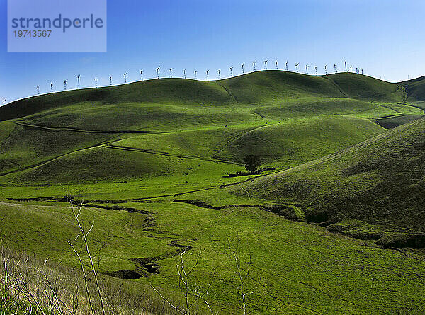 Wind turbines line a mountain ridge above a fertile farming valley