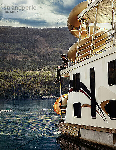 Mann genießt ein Hausboot  einen Familienurlaub und angelt vom Deck aus  während er am Ufer des Shuswap Lake parkt; Shuswap Lake  British Columbia  Kanada