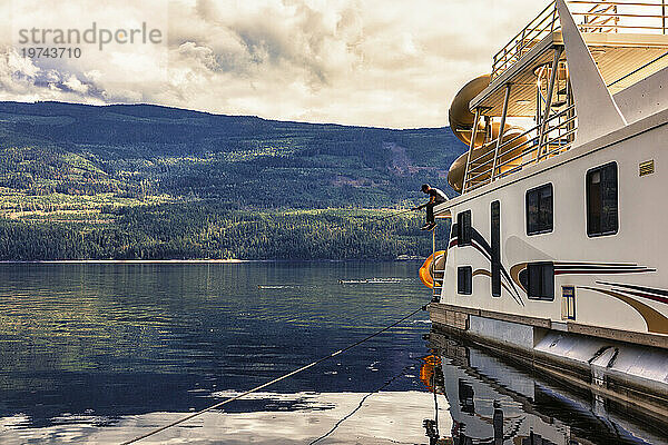 Mann genießt einen Familienurlaub  einen Hausbooturlaub und angelt vom Deck des Hausboots aus  während er am Ufer des Shuswap Lake parkt; Shuswap Lake  British Columbia  Kanada