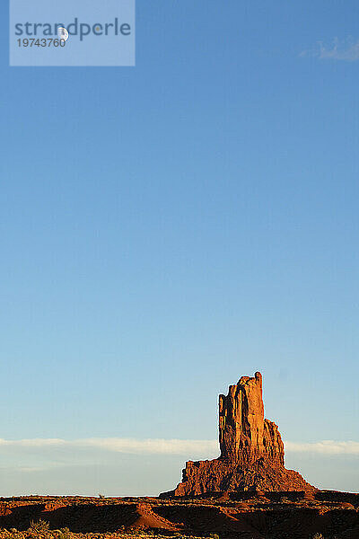 Felsformation im Monument Valley  Arizona  mit dem Mond am klaren blauen Himmel. Der rote Felsen leuchtet bei Sonnenuntergang  wenn das Licht auf ihn trifft. Arizona  Vereinigte Staaten von Amerika