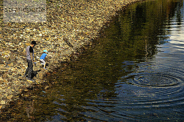 Ein Vater und seine kleine Tochter hüpfen im Urlaub über Steine ??an der Küste; Shuswap Lake  British Columbia  Kanada