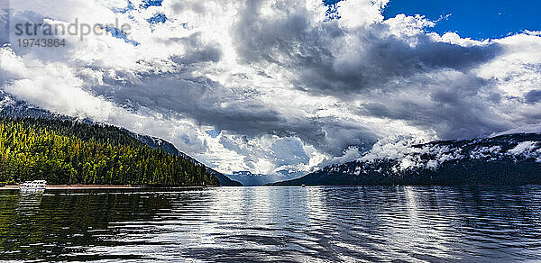 Malerische Aussicht auf den wunderschönen Shuswap-See mit dramatischen Wolken am Himmel und einem am Ufer vertäuten Hausboot und einem Boot auf dem Wasser während der Herbstsaison; Shuswap Lake  British Columbia  Kanada