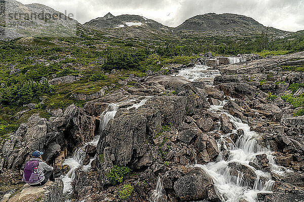 Blick von hinten auf eine Frau  die auf einer felsigen Klippe über den Wasserfällen entlang des International Falls Trail sitzt  einer der großartigsten Wanderungen im Yukon-Gebiet; Yukon  Kanada