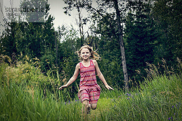 Porträt eines jungen Mädchens  das durch das Gras in einem Park rennt und in die Kamera lächelt; Edmonton  Alberta  Kanada