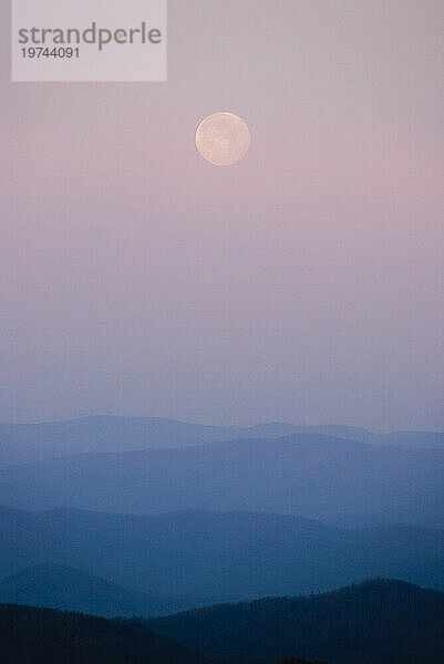 Vollmond in einem rosa Himmel über Schichten von Silhouetten von Bergen