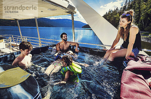 Eine Gruppe von Familienmitgliedern genießt einen Hausbooturlaub  während sie am Ufer des Shuswap Lake parken und im Whirlpool des Bootes sitzen; Shuswap Lake  British Columbia  Kanada