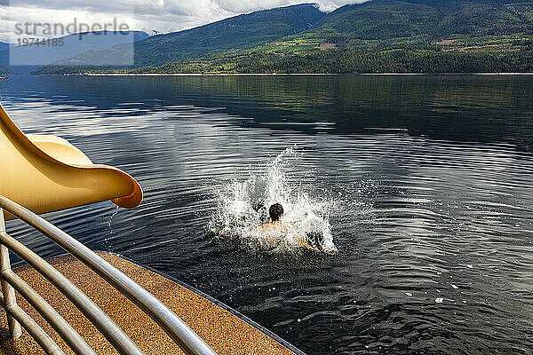 Junge planscht ins Wasser  nachdem er an einem Herbsttag auf dem Shuswap Lake aus dem Ende einer Hausboot-Wasserrutsche gerutscht ist; British Columbia  Kanada