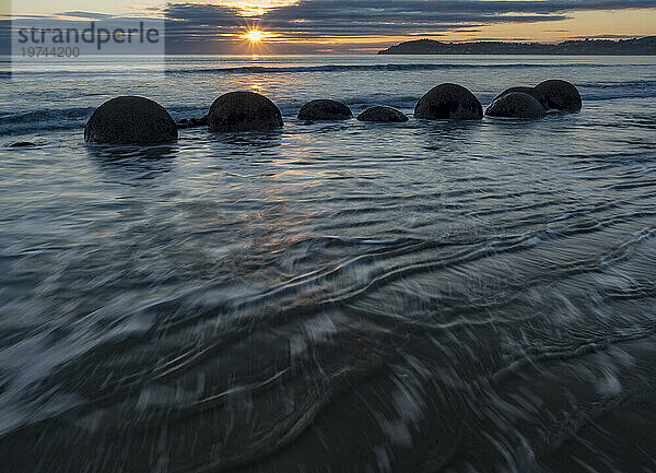 Einströmende Flut bei Sonnenaufgang mit den Moeraki-Felsbrocken in der Brandung entlang eines Abschnitts des Koekohe Beach auf der Südinsel Neuseelands; Hampden  North Otago  Neuseeland