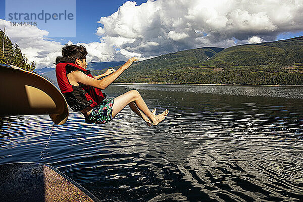 Junge rutscht an einem Herbsttag auf dem Shuswap Lake auf einem Hausboot aus dem Ende einer Wasserrutsche; British Columbia  Kanada