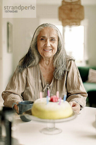 Porträt einer lächelnden älteren Frau mit Geburtstagstorte auf dem heimischen Tisch