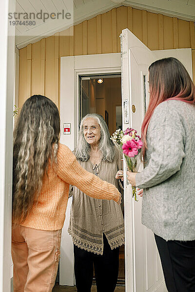 Glückliche Seniorin begrüßt Tochter und Enkelin am Eingang des Hauses