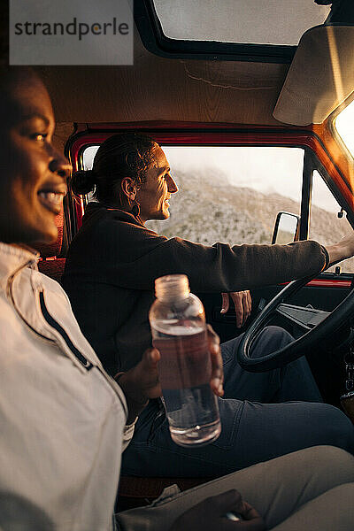 Junger Mann fährt Lieferwagen  während er mit einer Freundin sitzt  die eine Wasserflasche hält