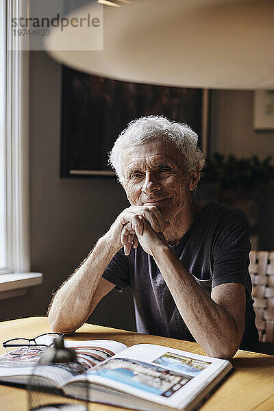 Porträt eines lächelnden älteren Mannes mit der Hand am Kinn  der zu Hause sitzt