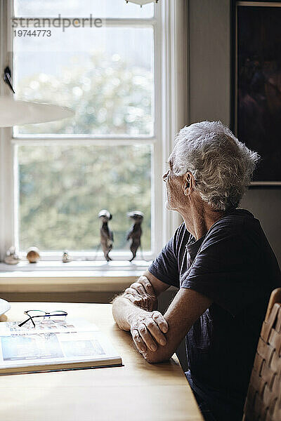 Älterer Mann schaut durch das Fenster  während er zu Hause sitzt
