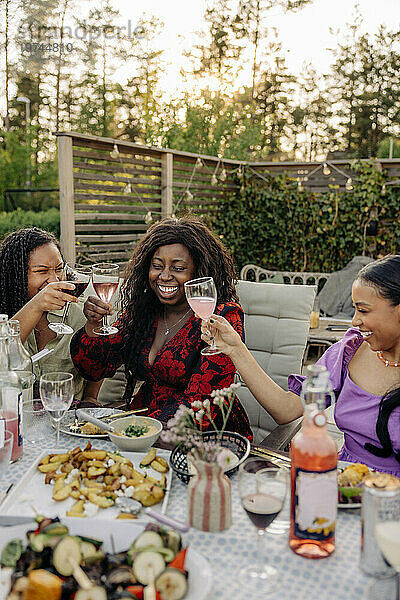 Fröhliche Freundinnen stoßen während der Dinnerparty am Esstisch auf Getränke an