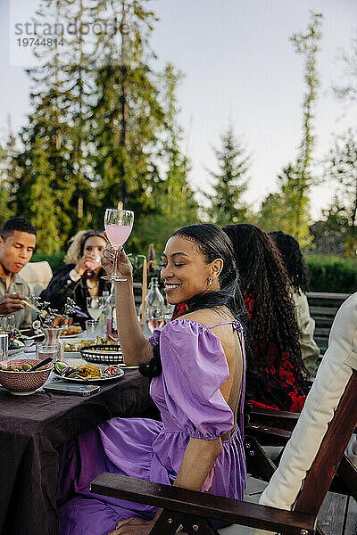 Seitenansicht einer lächelnden Frau  die während einer Dinnerparty mit Freunden ein Glas Glas in der Hand hält