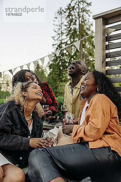 Fröhliche männliche und weibliche Freunde lachen  während sie während der Party etwas trinken