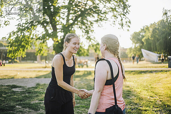 Lächelnde Frau beim Händeschütteln mit Freundin im Park