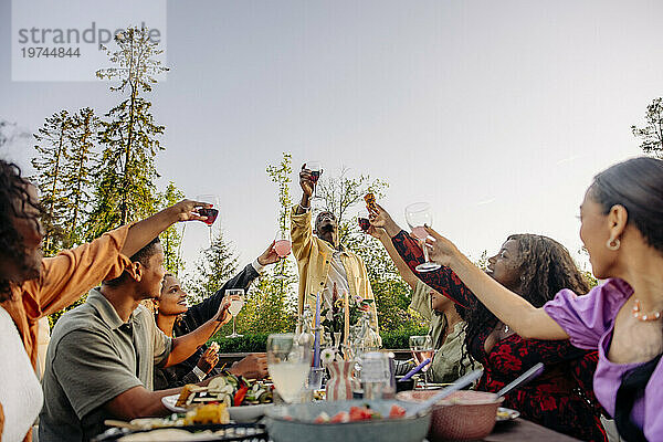 Gemischtrassige männliche und weibliche Freunde stoßen Getränke an  während sie während der Dinnerparty im Hinterhof feiern