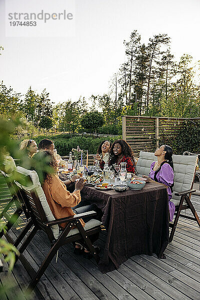 Fröhliche männliche und weibliche Freunde genießen gemeinsam die Dinnerparty am Esstisch im Hinterhof