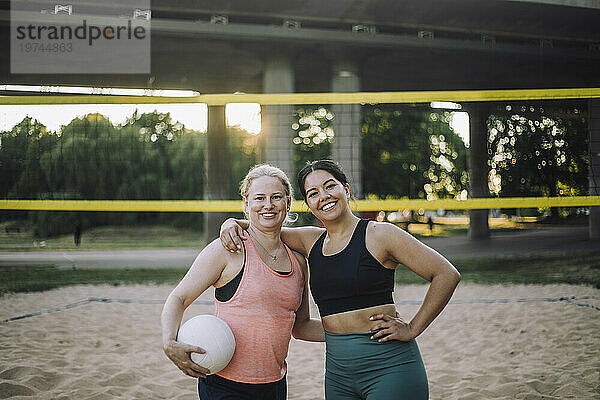 Porträt einer lächelnden Frau mit dem Arm um ihre Freundin  die Volleyball hält