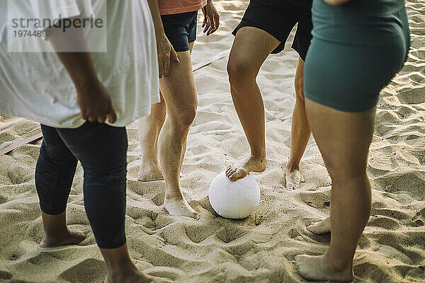 Unterer Abschnitt von Freundinnen  die mit Volleyball auf Sand stehen