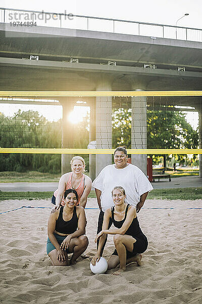 Porträt lächelnder Frauen  die beim Volleyballspielen in der Nähe des Netzes posieren