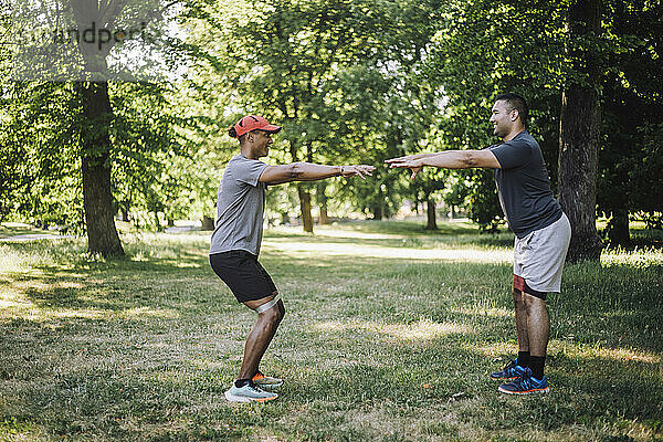 Seitenansicht männlicher Freunde  die gemeinsam auf Gras im Park trainieren