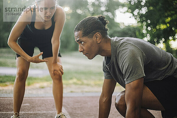 Weibliche Trainerin leitet entschlossenen Mann an  der sich auf den Sprint auf der Laufstrecke vorbereitet