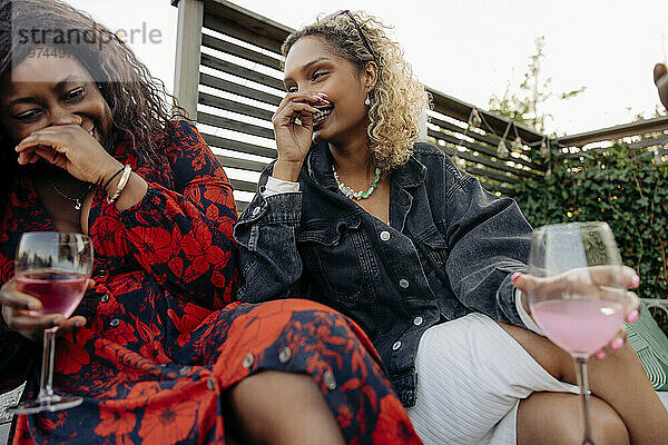 Junge Freundinnen lachen  während sie während der Party im Hinterhof Getränkegläser halten