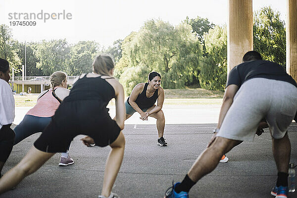 Lächelnde Frau beim Stretching mit männlichen und weiblichen Freunden während des Trainings