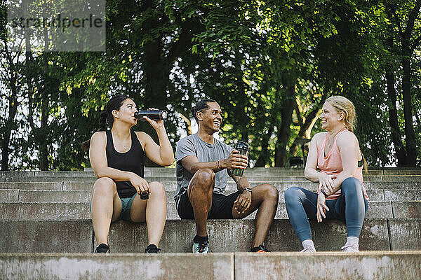 Low-Angle-Ansicht lächelnder männlicher und weiblicher Freunde  die während der Pause nach dem Training im Sitzen Wasser trinken und reden