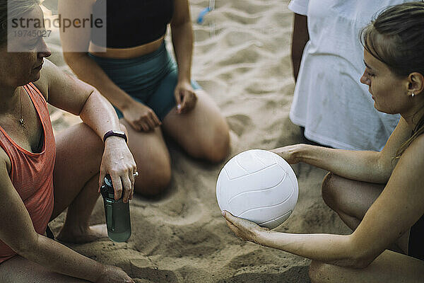 Blick aus der Vogelperspektive auf eine Frau  die Volleyball spielt  während ihre Freunde im Sand knien