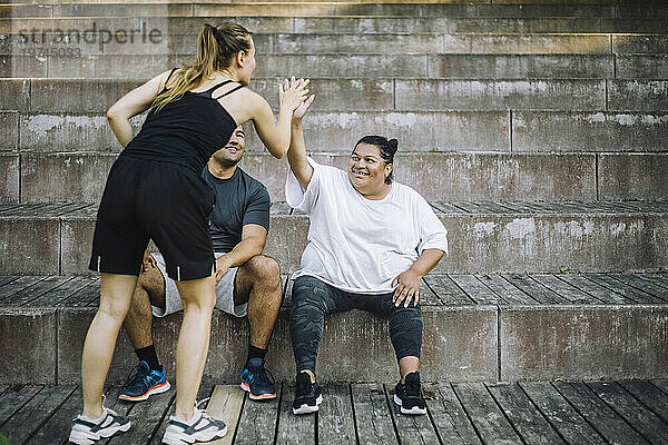 Junge Frau gibt einer Frau  die mit einem männlichen Freund auf der Treppe sitzt  High-Five