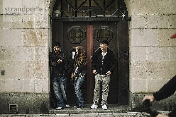 Glückliche männliche und weibliche Teenager-Freunde lachen  während sie in der Nähe der Gebäudetür stehen