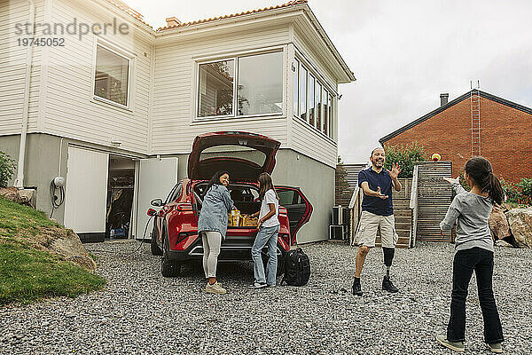Glückliche Familie  die Spaß hat  während sie neben dem Elektroauto am Haus steht