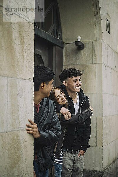 Lächelndes Mädchen umarmt einen männlichen Teenager-Freund  der in der Nähe eines Gebäudes steht