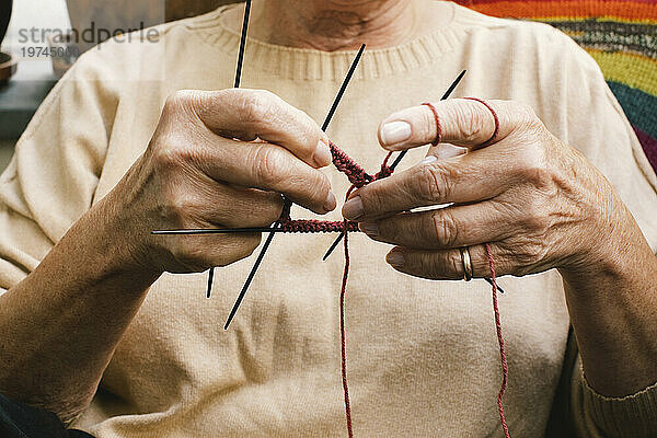 Mittelteil einer älteren Frau  die strickt  während sie zu Hause sitzt