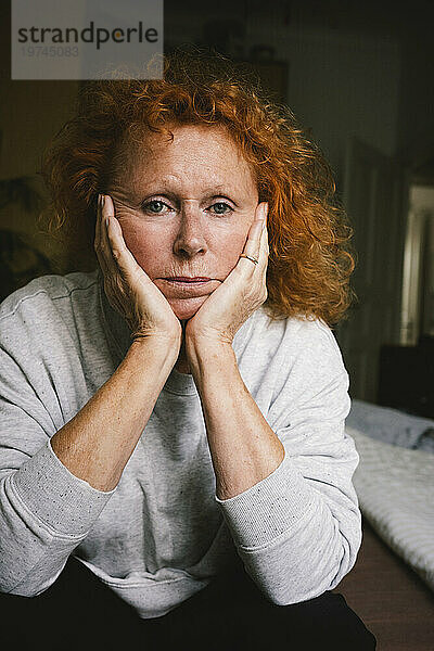 Porträt einer depressiven älteren Frau  die mit dem Kopf in den Händen zu Hause sitzt