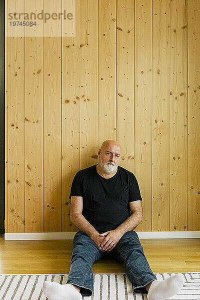 Verärgerter reifer Mann sitzt zu Hause in der Nähe einer Holzwand