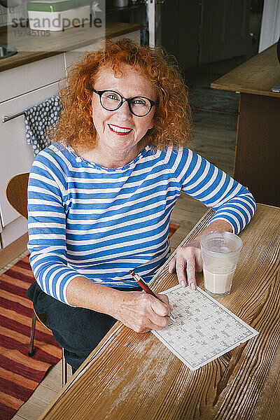 Portrait of smiling senior woman with sudoku while sitting at table
