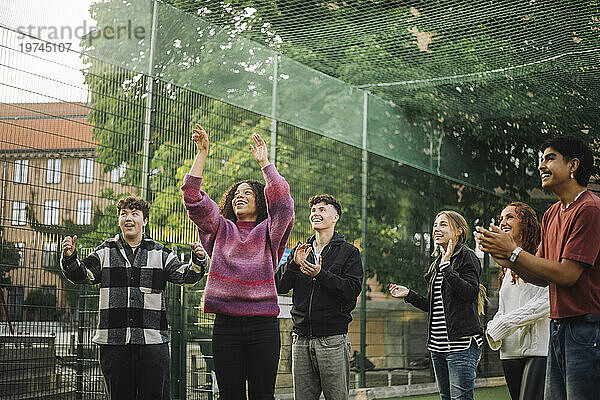 Fröhliche Freunde jubeln einem Teenager-Mädchen zu  das auf dem Platz Basketball spielt