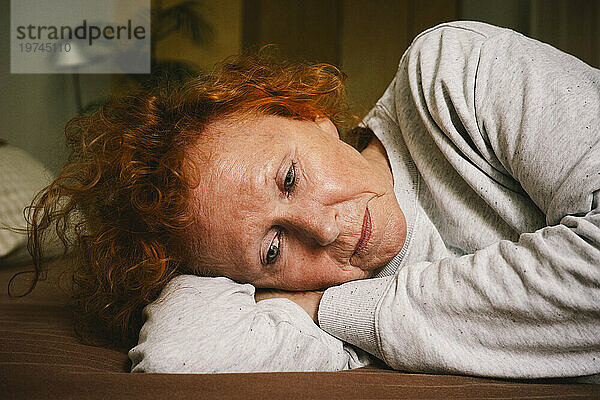 Traurige ältere Frau denkt nach  während sie zu Hause im Bett liegt