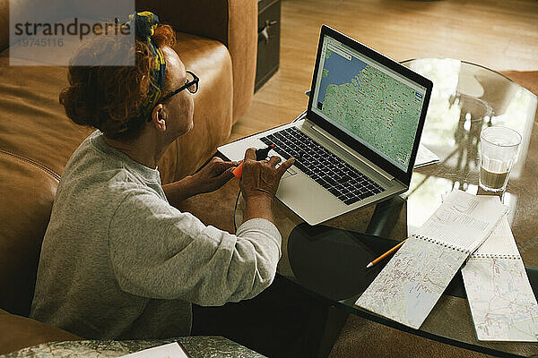 Seitenansicht einer älteren Frau  die zu Hause eine Reise auf der Karte im Laptop plant