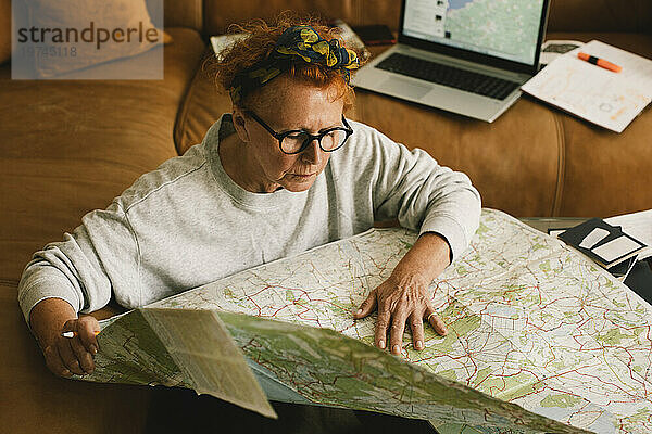 Blick aus der Vogelperspektive auf eine ältere Frau  die auf der Karte im Wohnzimmer eine Reise plant