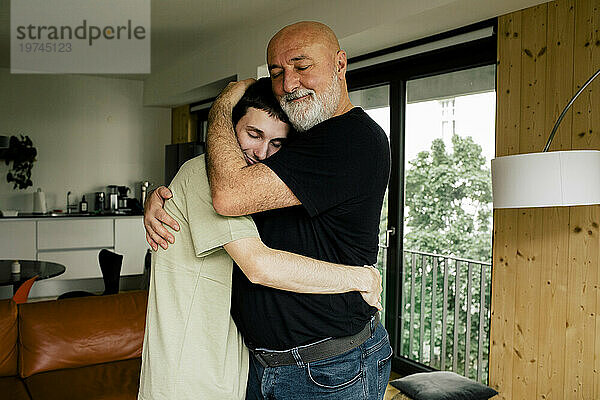 Seitenansicht eines lächelnden Mannes  der seinen Sohn umarmt  während er zu Hause steht