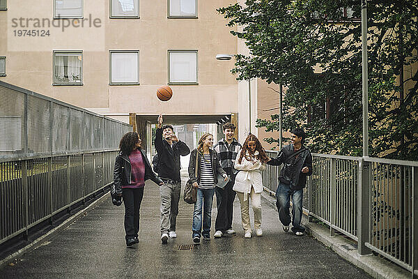 Junge spielt Basketball  während er mit männlichen und weiblichen Freunden auf dem Fußweg spaziert