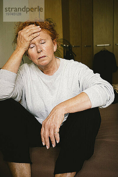 Besorgte ältere Frau sitzt mit dem Kopf in der Hand zu Hause